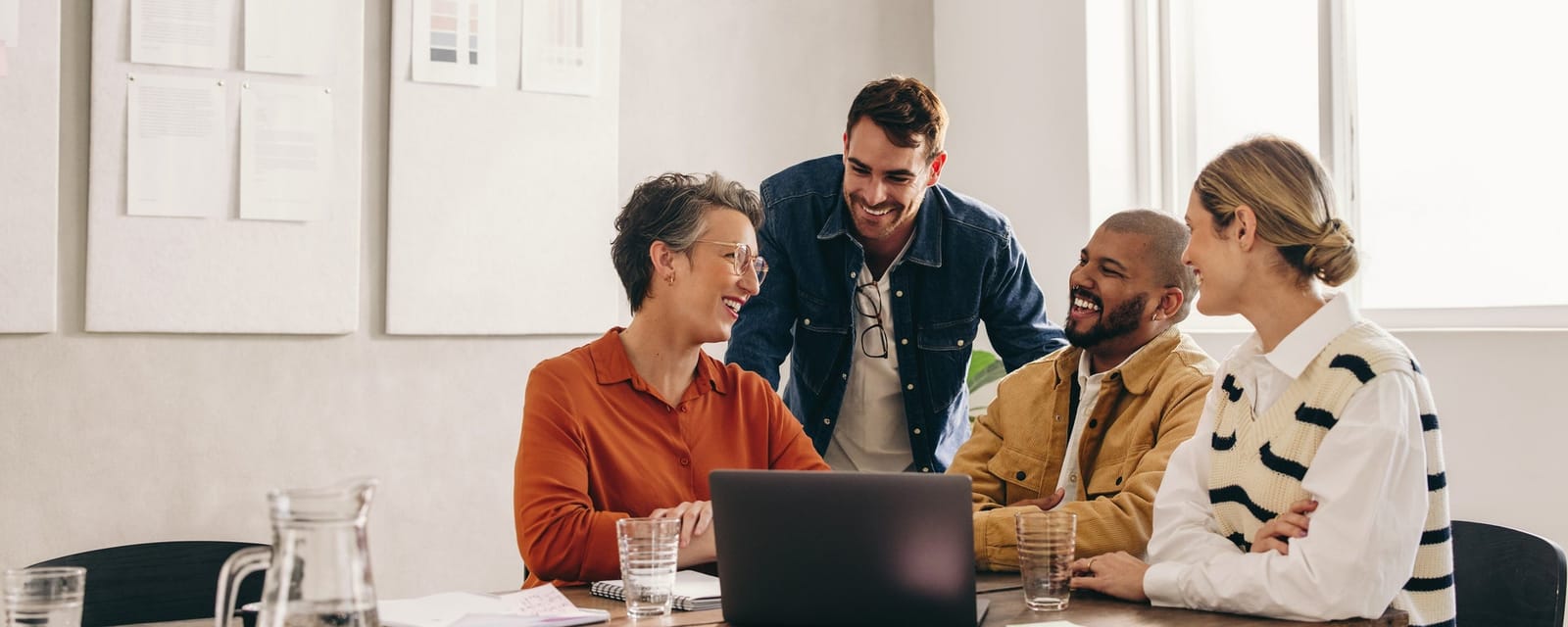 Coworkers laughing in front of a laptop in a casual office setting